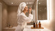 Woman in a towel applying skincare at a bathroom mirror